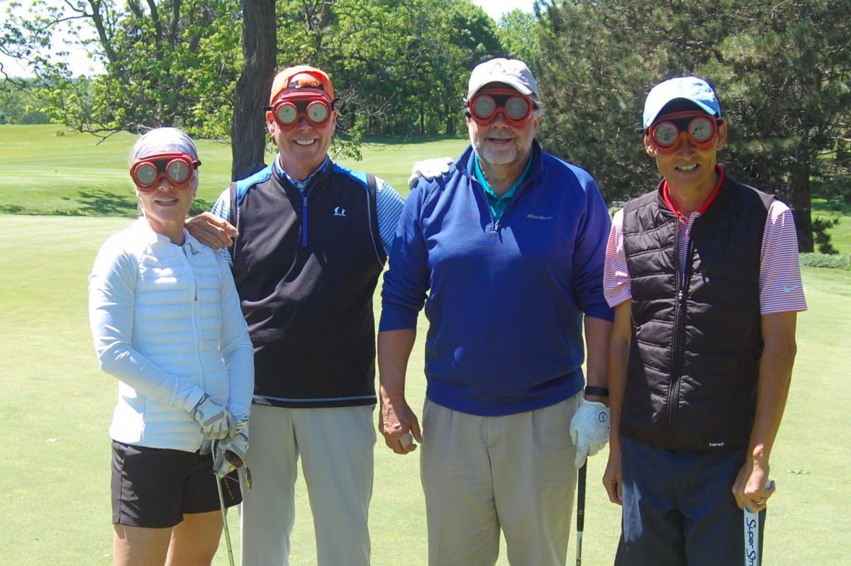 Four People posing on the golf course while wearing protective eye gear