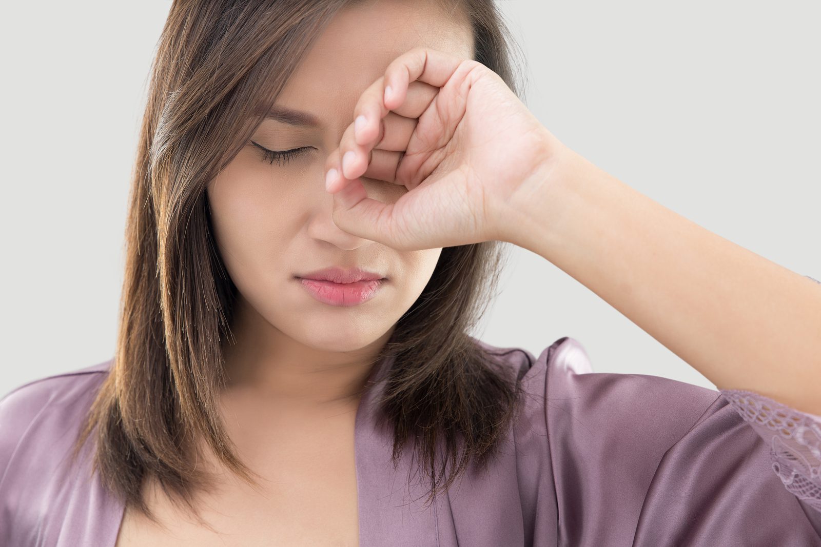 A photo of a woman rubbing her eye as if it's irritated
