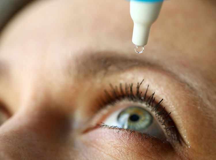 a woman putting drops in her eye.