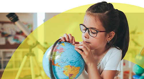a child in school wearing glasses, looking at a globe.